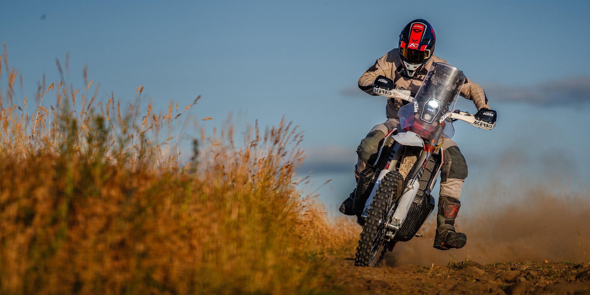 A rider leans the KTM 450 Rally Replica into a turn, dust rising in the evening light